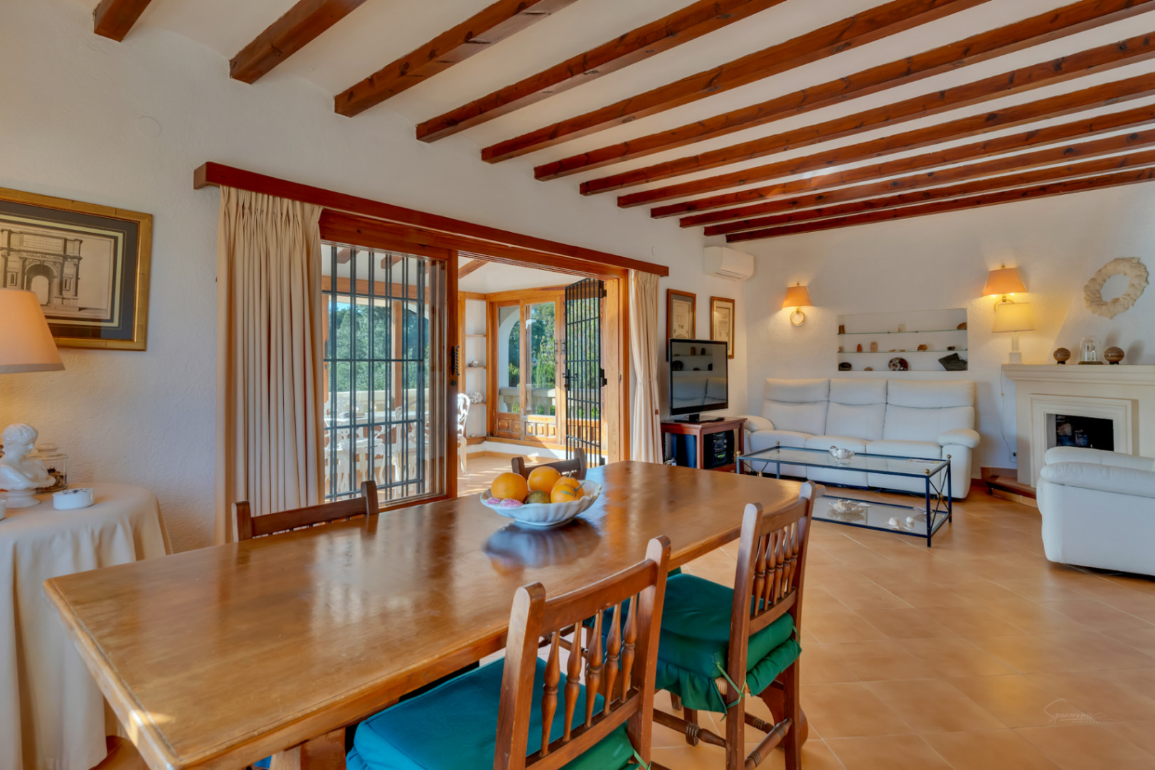 Mediterranean living and dining area featuring exposed wooden ceiling beams, terracotta floors, and access to a bright glazed terrace.