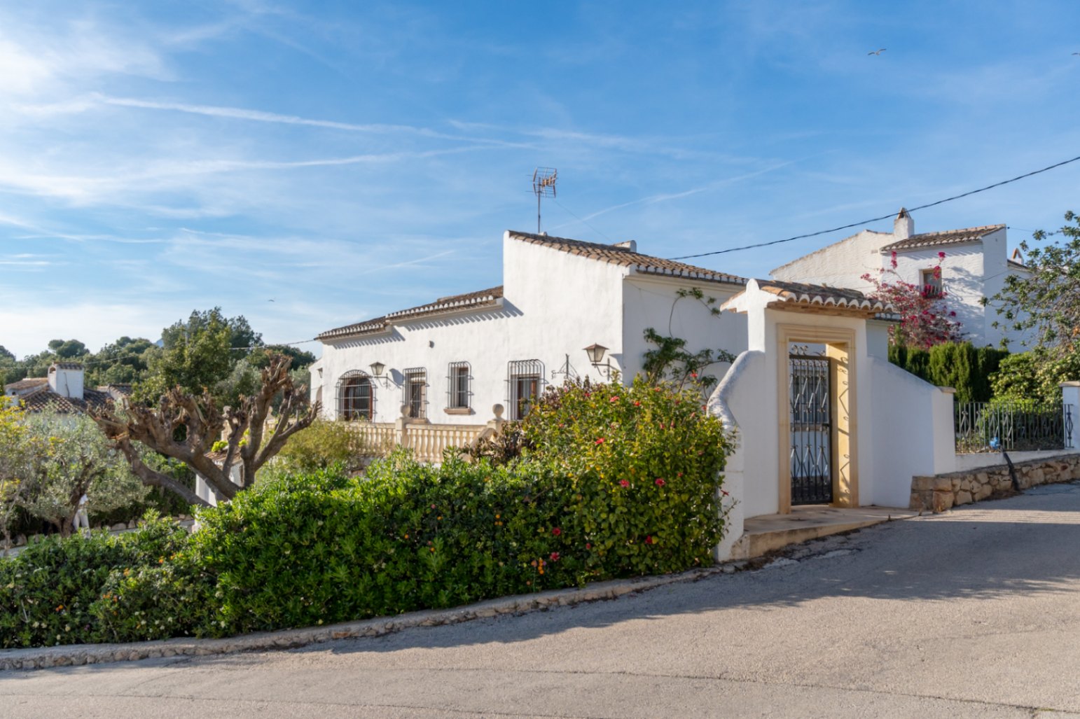Mediterranean-style exterior featuring white walls, wrought-iron window guards, and a pedestrian entrance with a traditional Tosca stone frame.