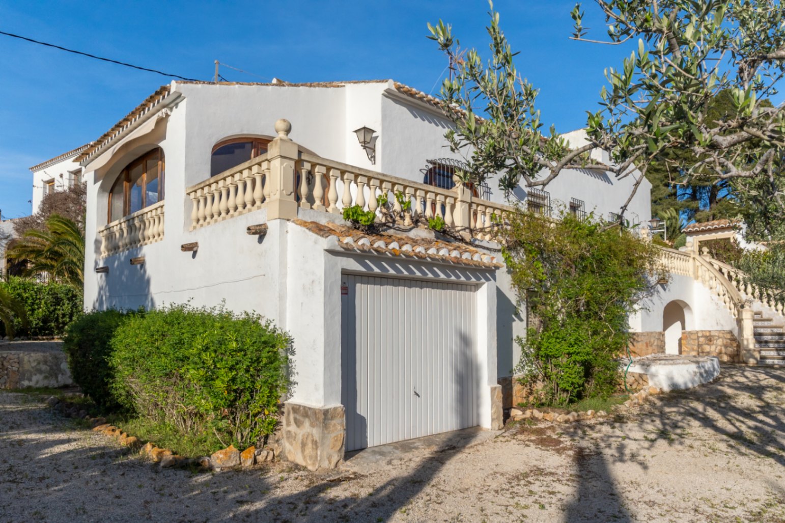 Mediterranean-style white facade featuring an integrated garage, traditional stone balustrade, and an exterior staircase with decorative ceramic tiling.