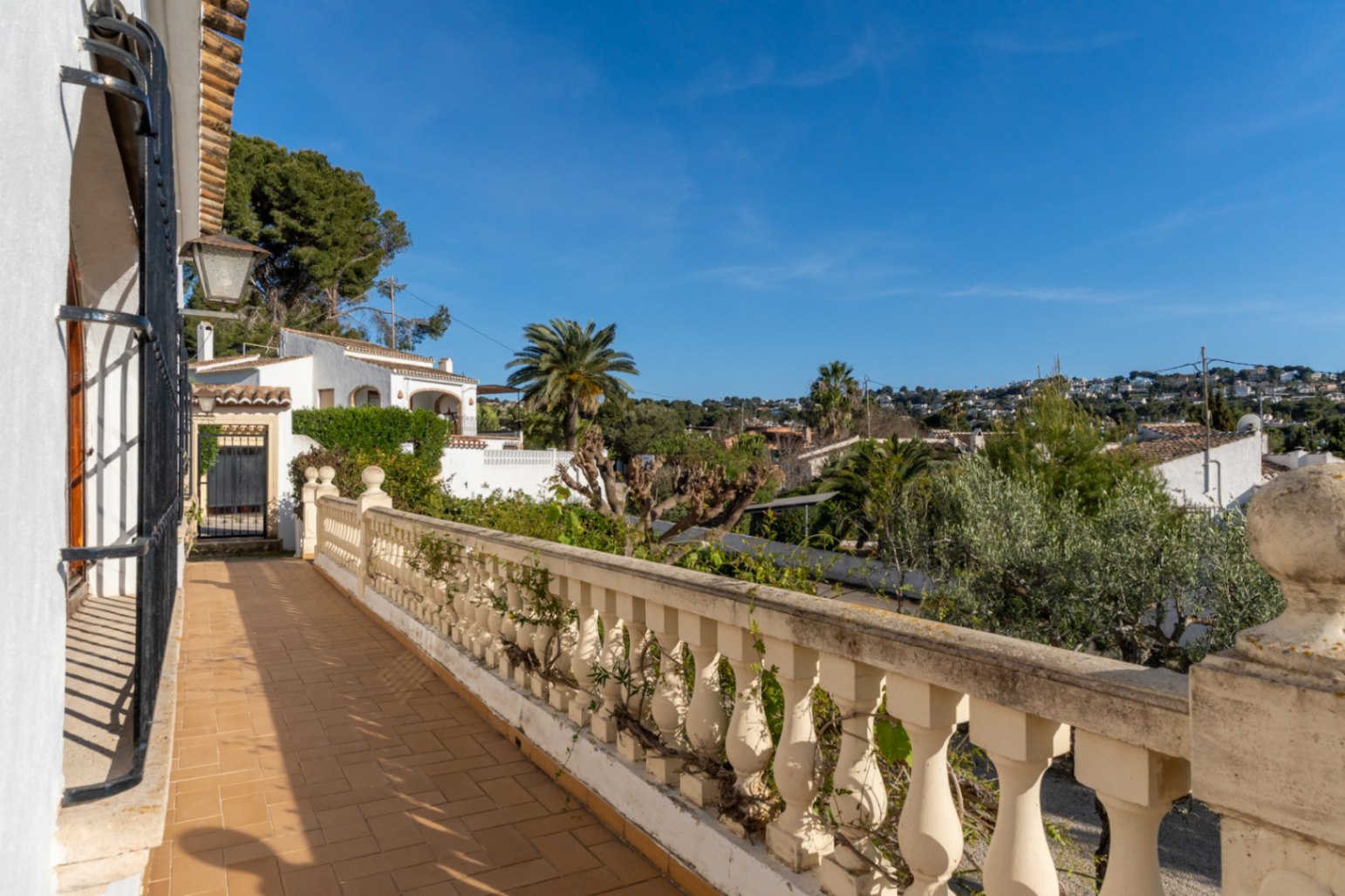 Outdoor terrace featuring traditional ceramic tiling and a classic balustrade, overlooking the residential landscape and Mediterranean greenery of Jávea.