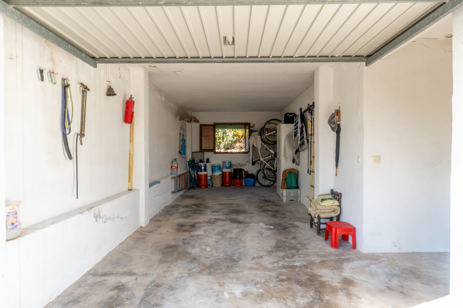 Spacious enclosed garage featuring concrete flooring and white walls, providing ample storage space and natural light through a rear window.
