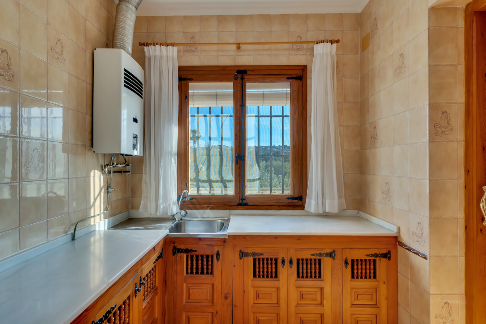 Traditional kitchen featuring carved wooden cabinetry, white countertops, and a wooden window frame that provides natural light and garden views.