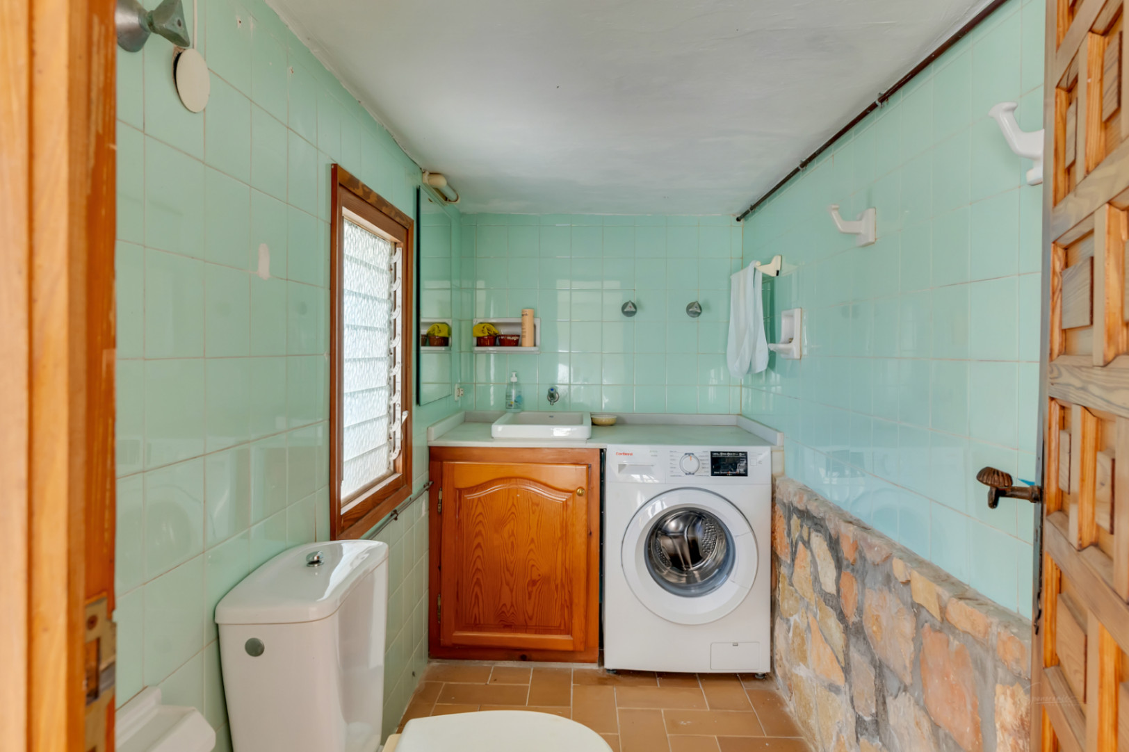 Utility room and guest toilet featuring mint green tiling, a natural stone accent wall, wooden cabinetry, and an integrated washing machine.