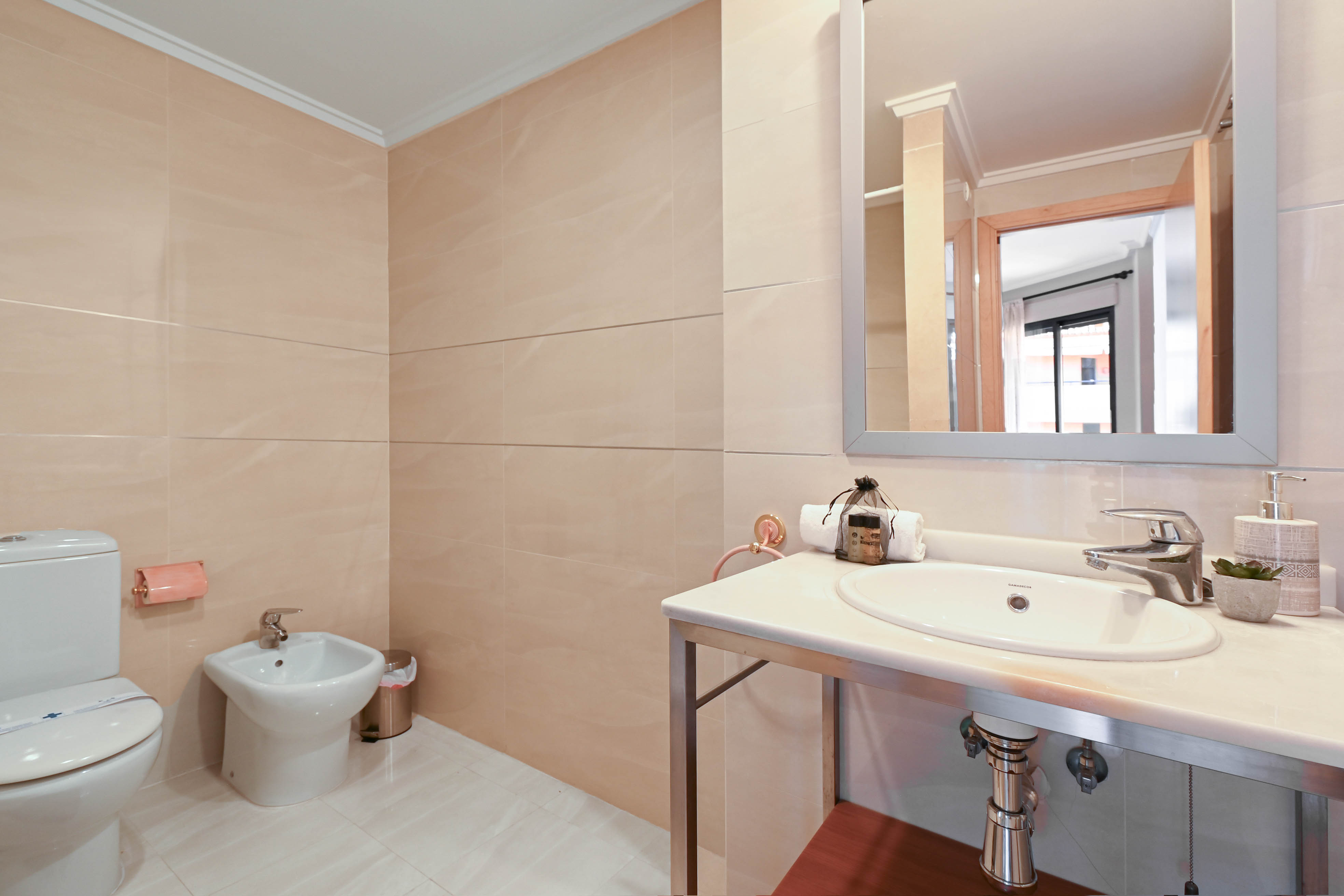 Bathroom featuring beige wall tiling, a bidet, and a white stone vanity with an integrated sink supported by a modern chrome frame.