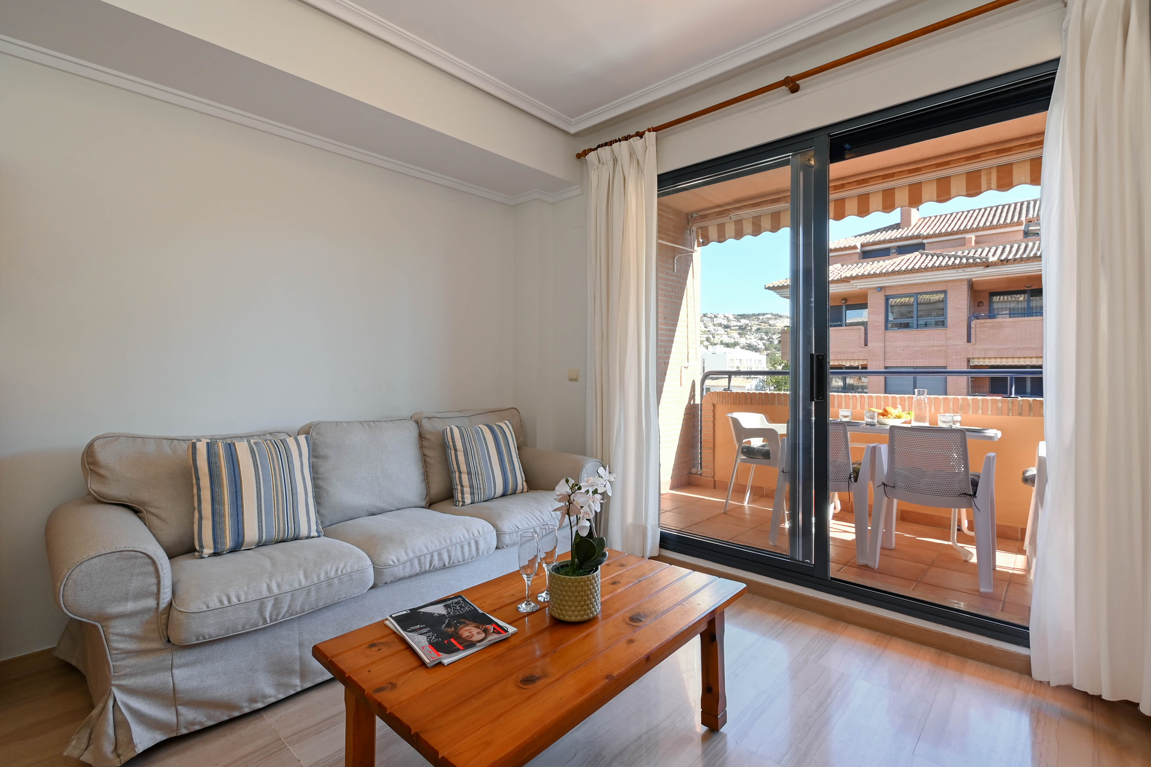 Bright living area featuring a grey sofa and wooden coffee table, with direct access through sliding glass doors to a furnished balcony.