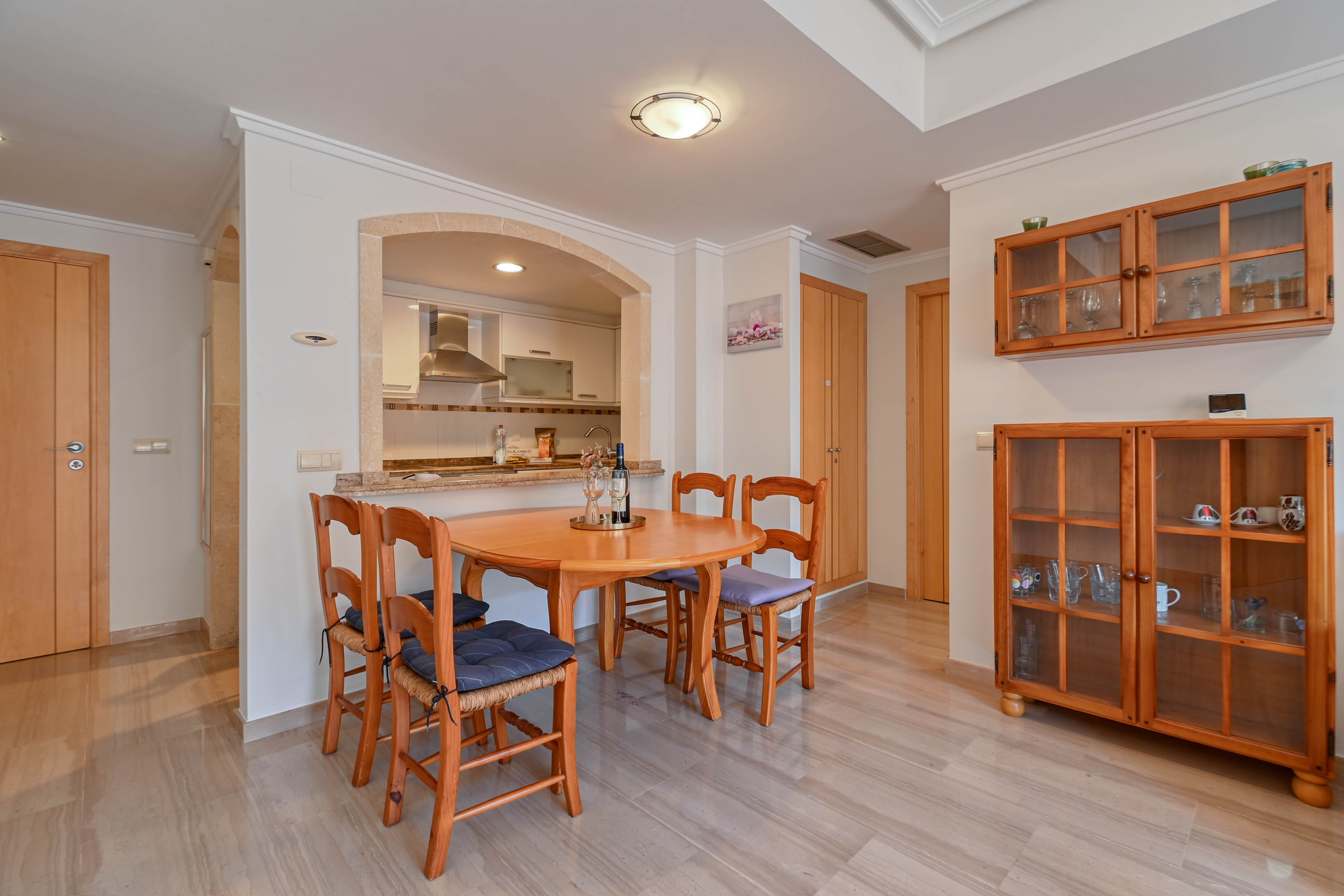 Dining area featuring a round wooden table and chairs, connected to the kitchen through a decorative stone archway over polished marble floors.