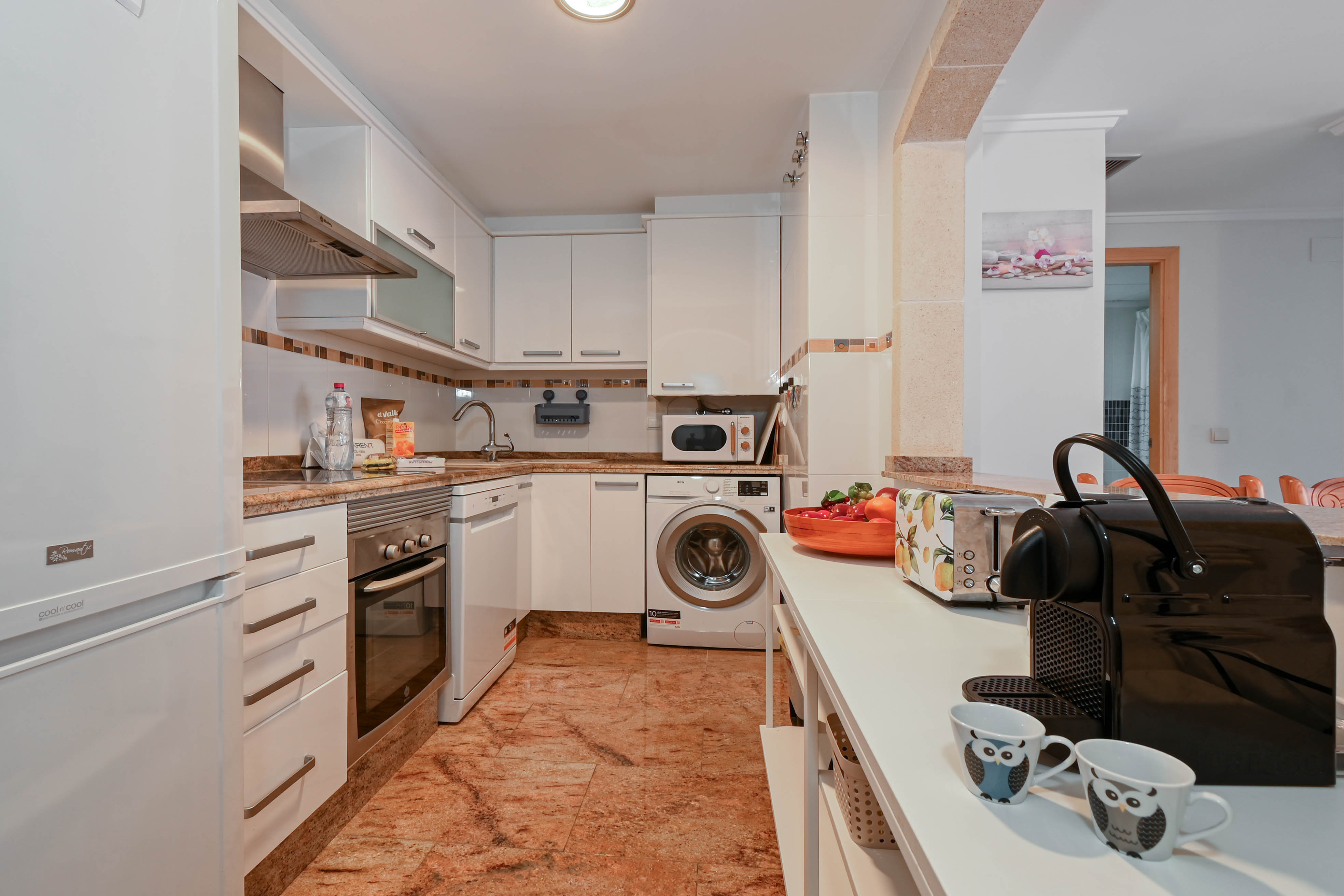 Fully equipped kitchen featuring white cabinetry, granite countertops, and integrated appliances including a washing machine, dishwasher, and coffee station.