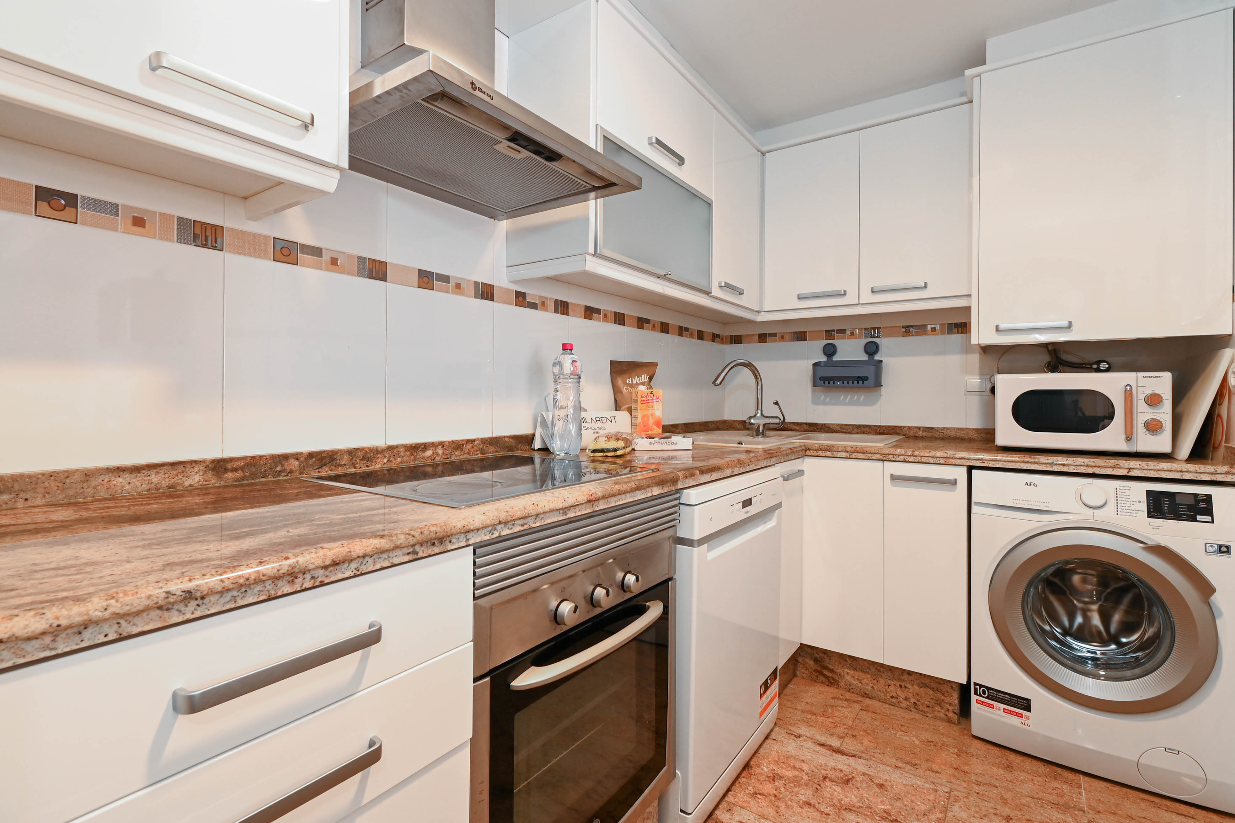 Functional kitchen featuring white cabinetry, granite countertops, and integrated appliances including a washing machine, dishwasher, and stainless steel oven.