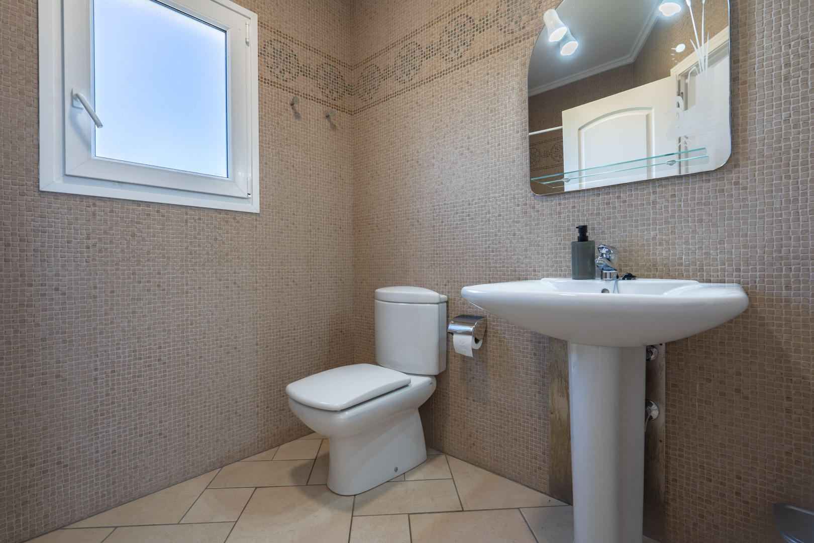 Bathroom featuring beige mosaic wall tiles, a classic pedestal sink, and a white PVC window for natural ventilation and light.