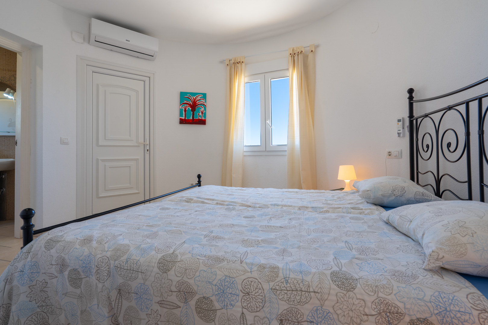 Bright bedroom featuring a black wrought-iron bed frame, air conditioning, PVC window, and direct access to an ensuite bathroom.
