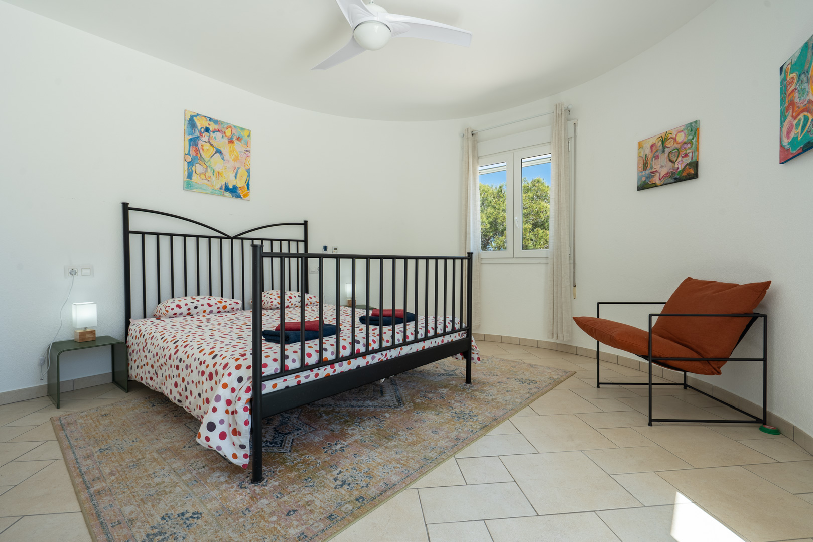 Bright bedroom featuring a curved wall, black metal bed frame, tiled flooring, and a PVC window overlooking the surrounding greenery.