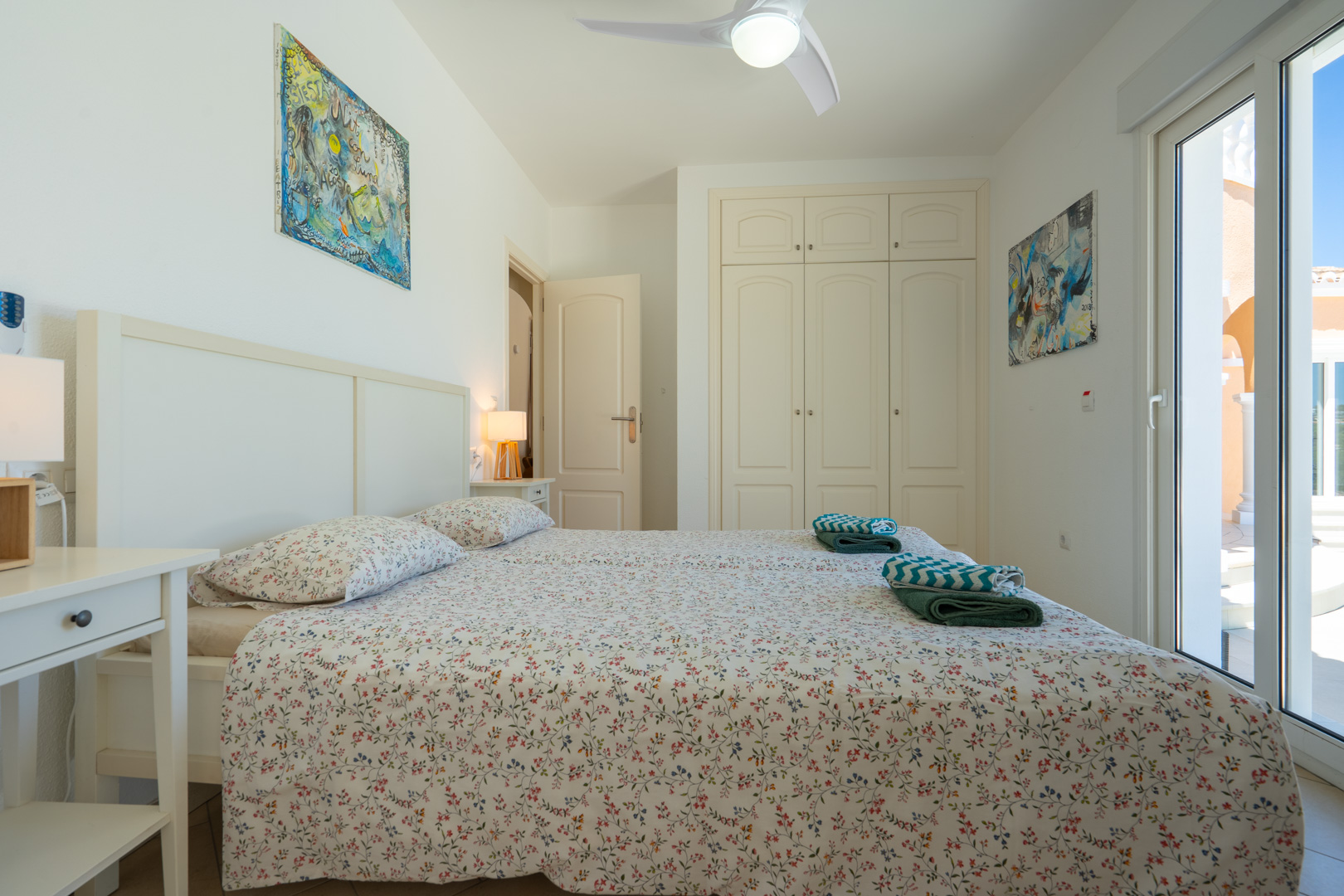 Bright bedroom featuring built-in wardrobes, a ceiling fan, and direct access to the terrace through double-glazed PVC sliding doors.