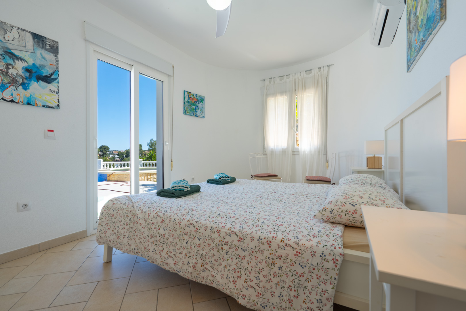 Bright bedroom featuring direct terrace and pool access, equipped with air conditioning, tiled flooring, and white PVC sliding doors.