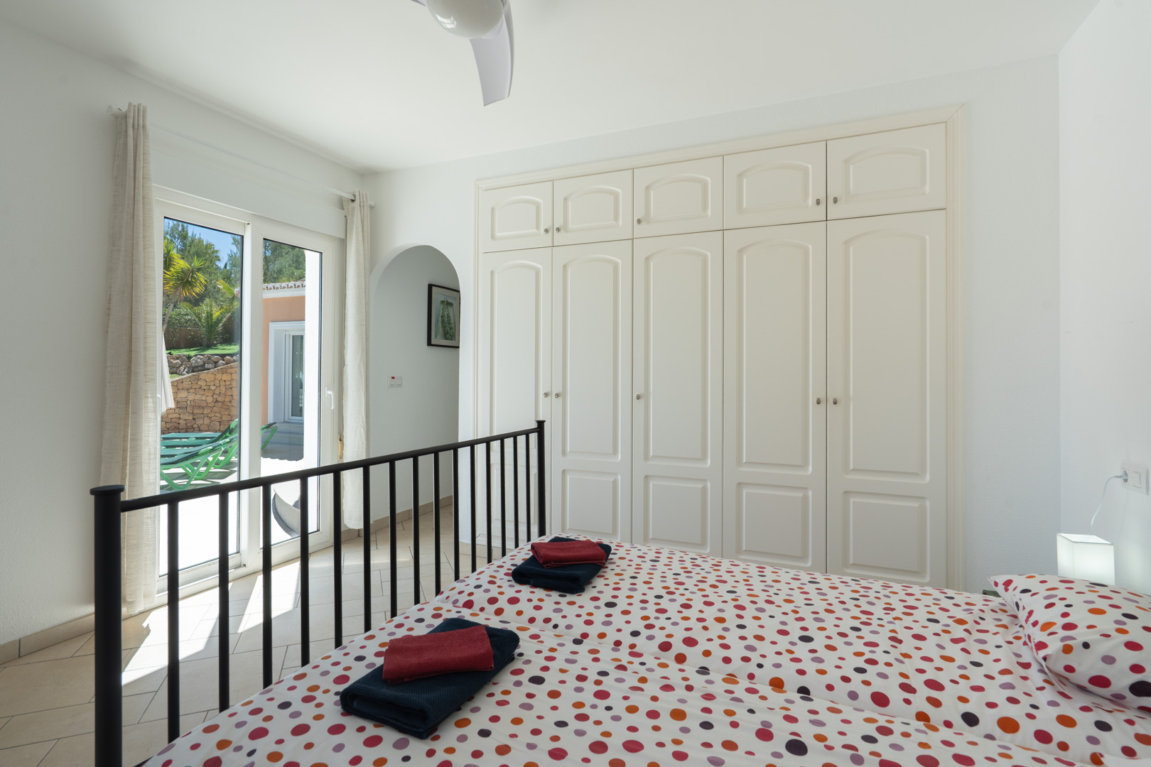 Bright bedroom featuring white built-in wardrobes, a ceiling fan, and direct access to the terrace through PVC sliding doors.