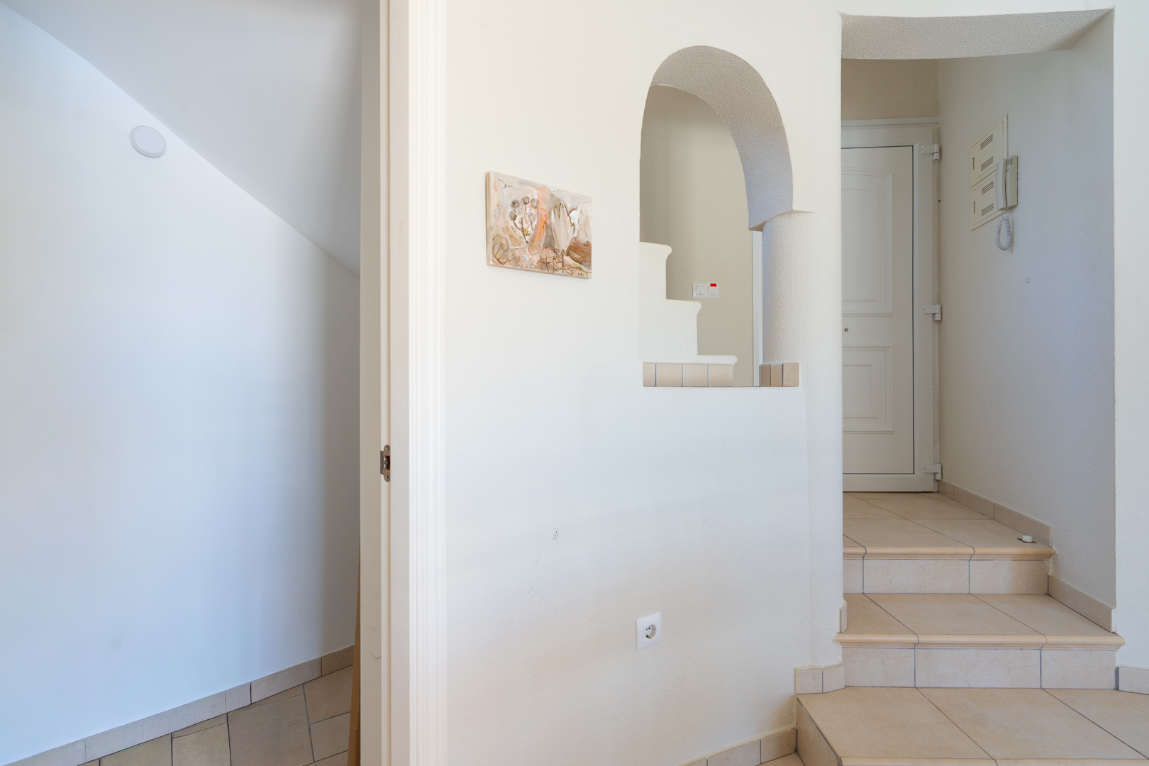 Entrance hall featuring a short interior staircase, neutral ceramic tiling, and a decorative arched wall opening leading to the upper level.