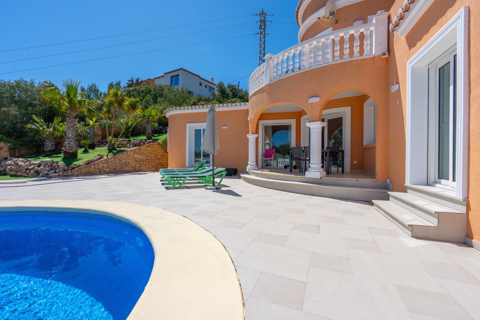 Exterior terrace featuring a curved swimming pool and an arched porch with white columns. The villa's terracotta facade is accented by classic balustrades and landscaped gardens.