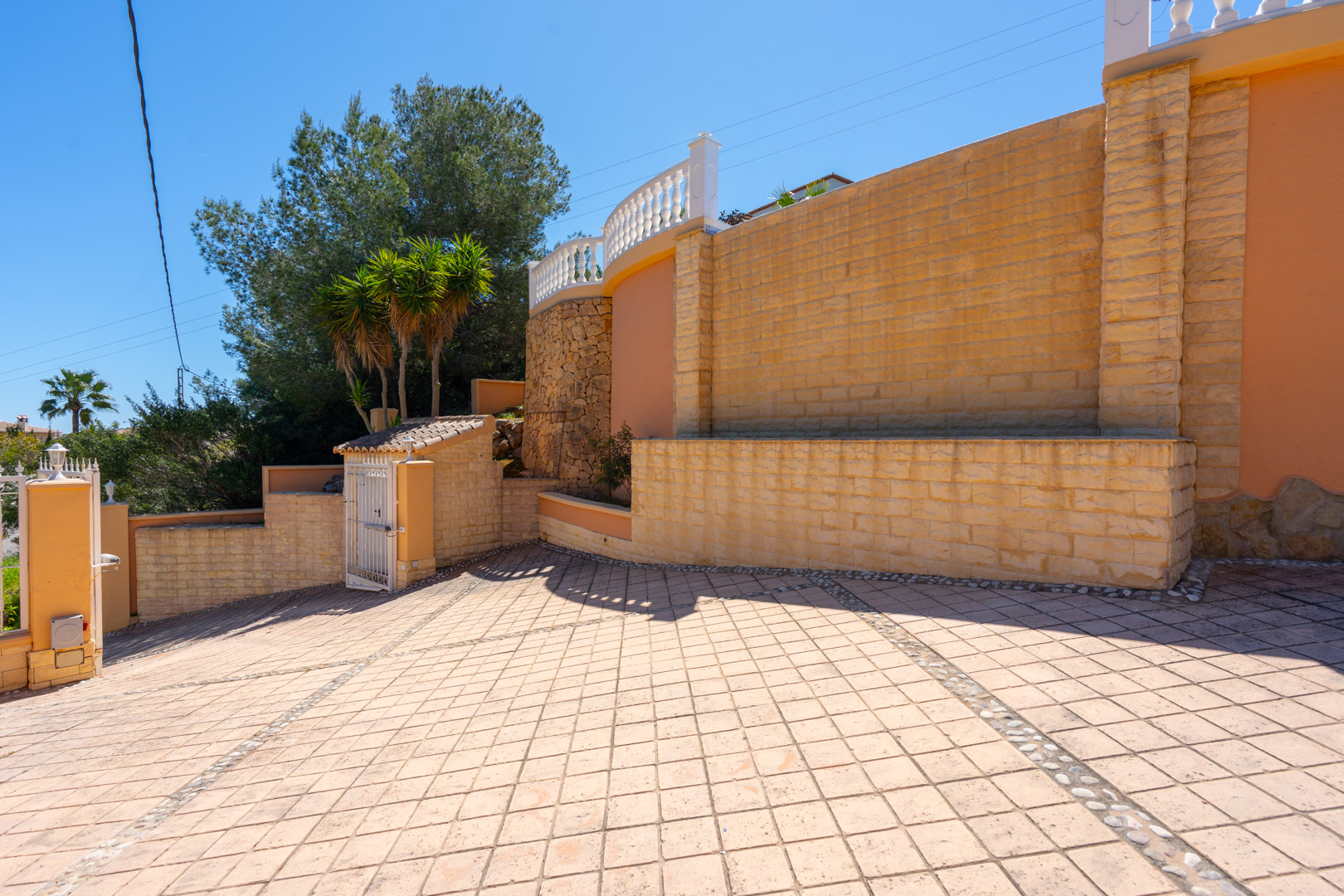 Main entrance featuring a spacious diamond-patterned paved driveway, natural stone retaining walls, and an upper terrace with classic white balustrades.