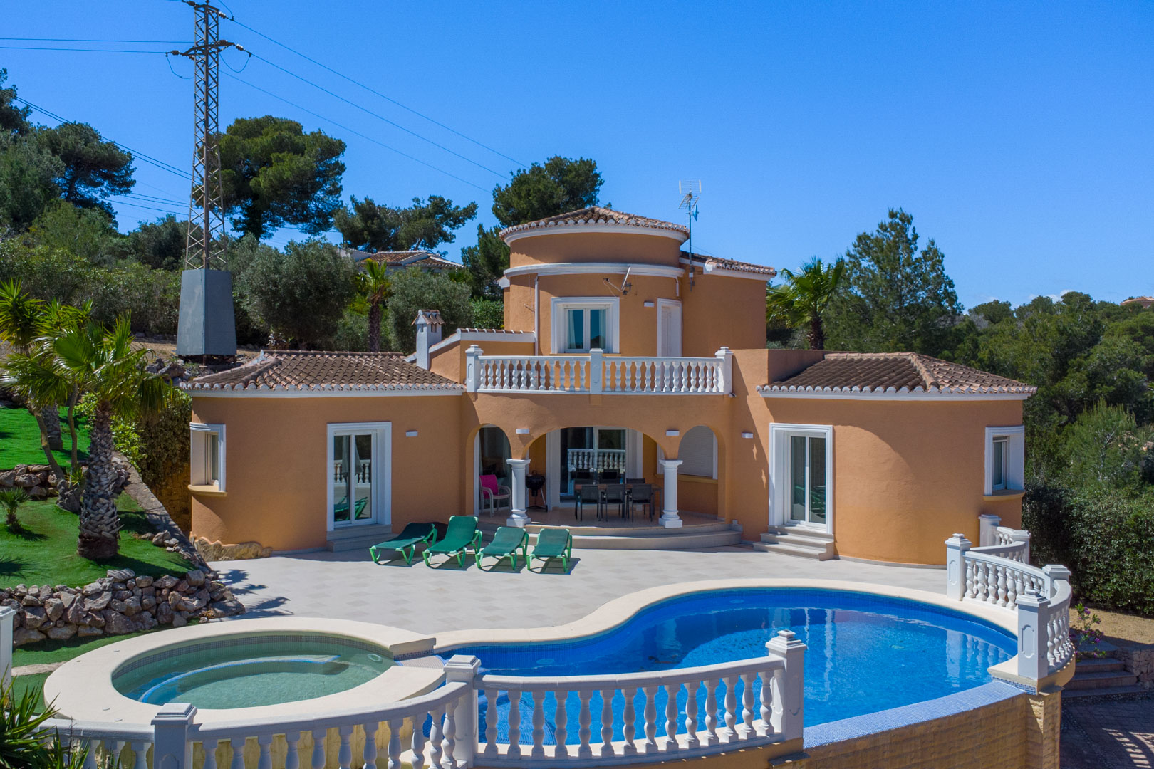 Mediterranean villa exterior featuring a curved swimming pool with an integrated spa, a spacious sun terrace, and a covered porch with white columns and balustrades.