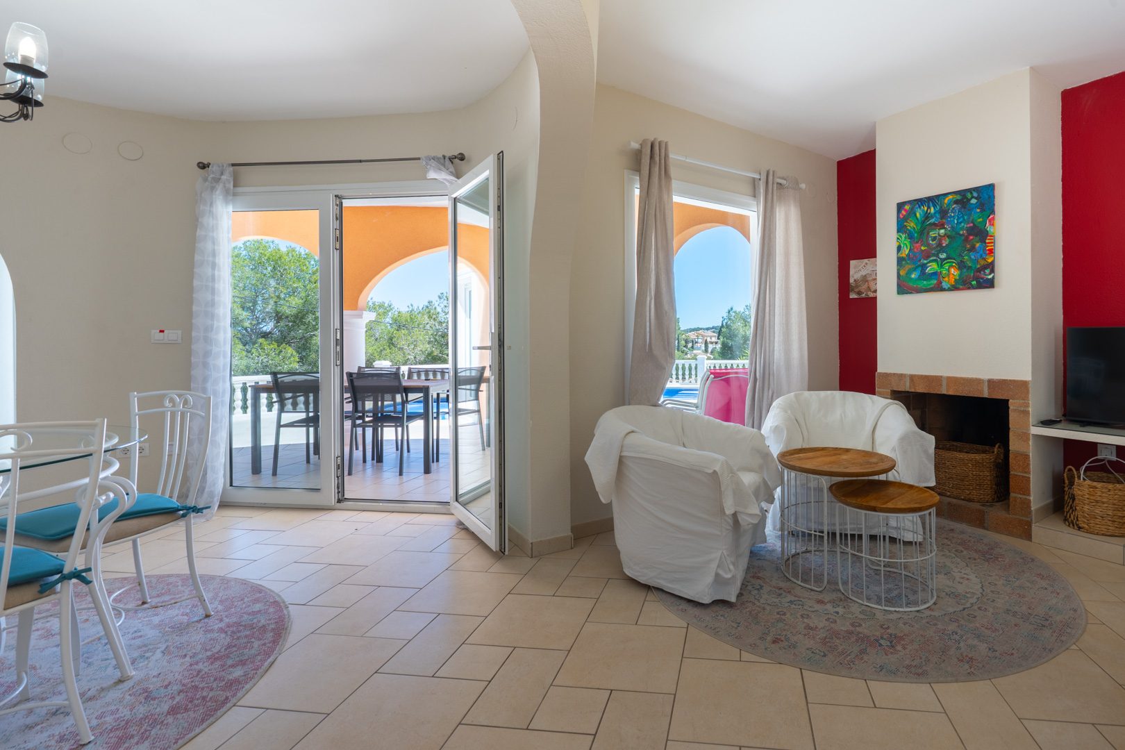 Open-plan living and dining area featuring a brick fireplace, ceramic flooring, and double-glazed PVC doors opening onto a covered terrace with pool views.