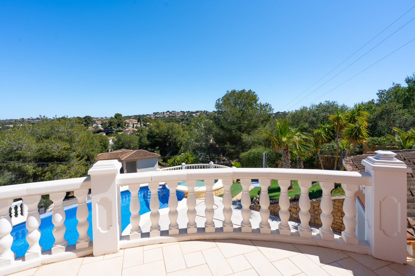Upper terrace featuring a classic white stone balustrade with views over the private pool, landscaped garden, and the verdant hills of Jávea.