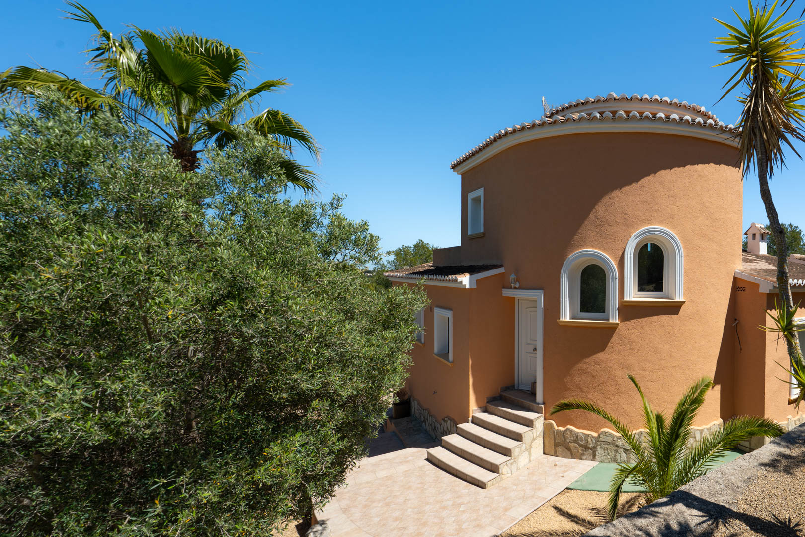 Villa exterior featuring a distinctive curved tower facade, arched windows with white frames, and stone steps leading to the main entrance.