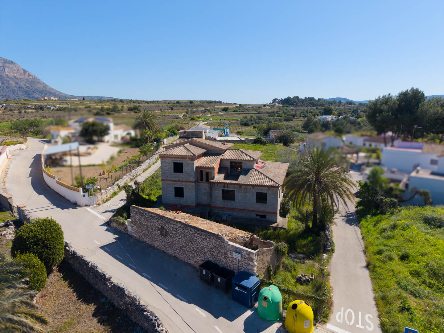 Aerial view of the concrete structure with tiled roofing, featuring stone perimeter walls and views of the Montgó mountain in the background.