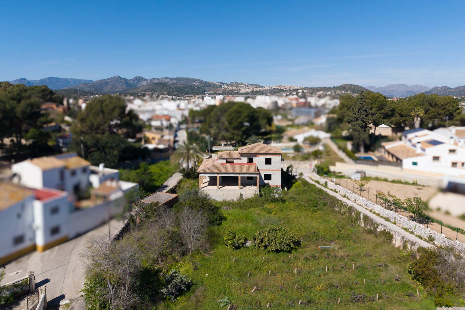 Aerial view of the unfinished residential structure with a terracotta roof, situated on a large 1,800 m² plot with mountain views and natural surroundings.