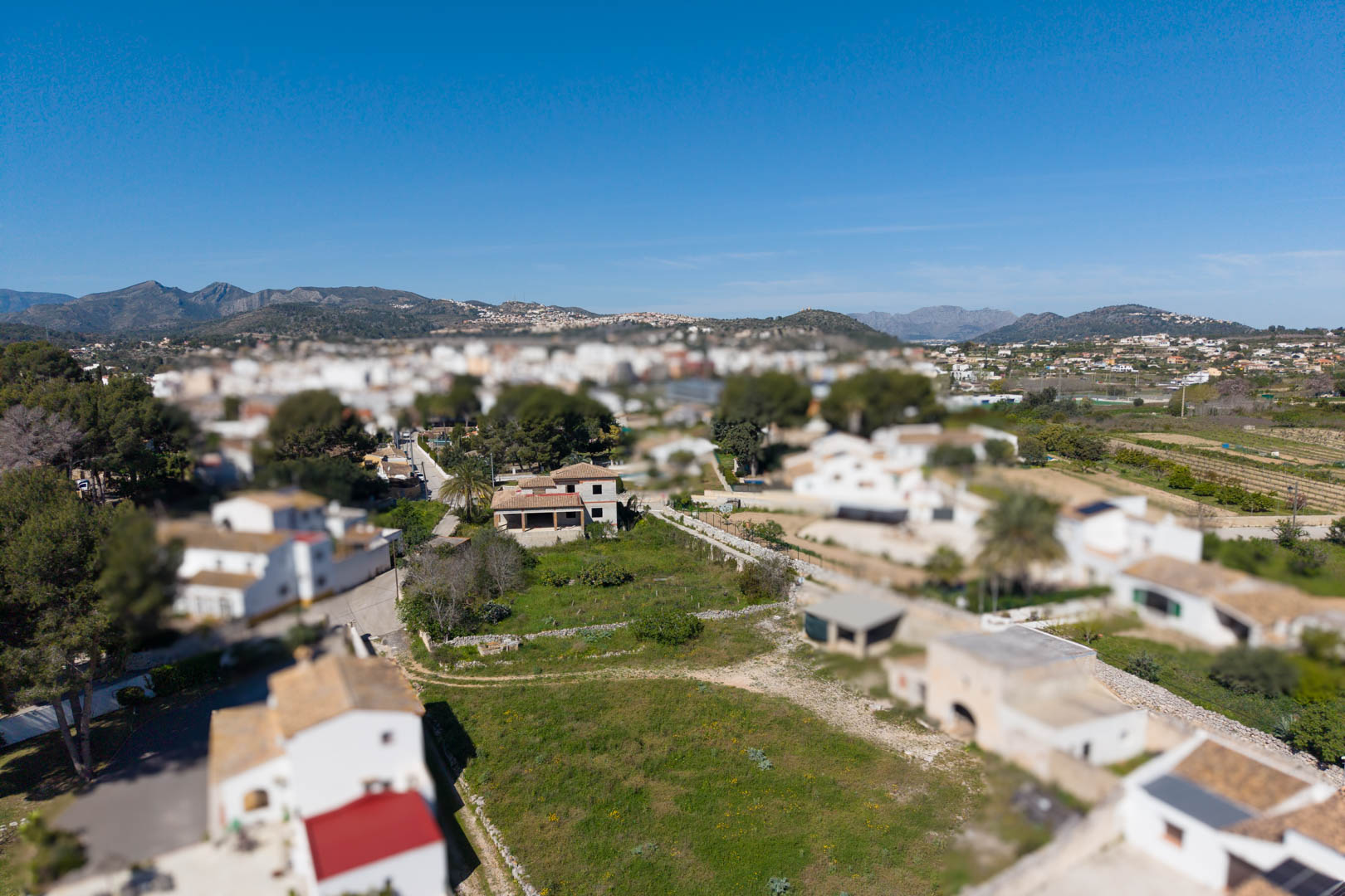 Aerial view showing the 1,800 sqm plot, the main house structure, and auxiliary buildings set against a backdrop of mountains and residential areas.