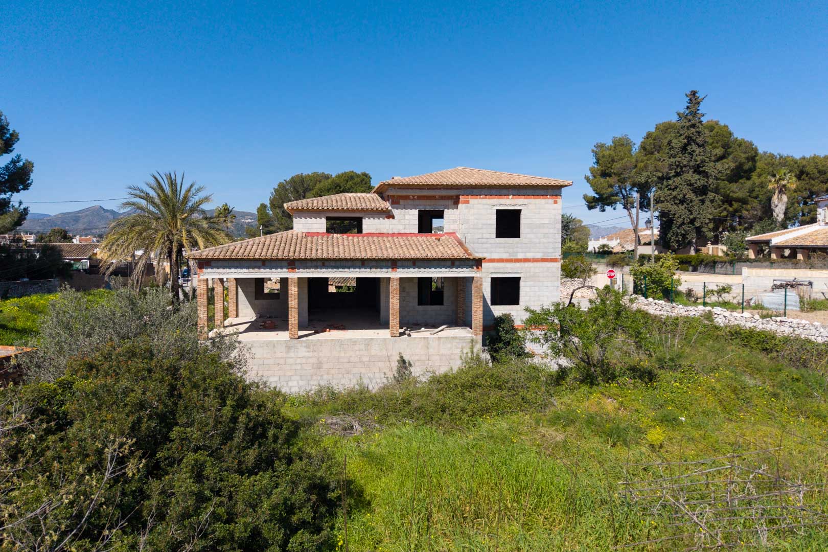 Two-story detached house structure featuring a ceramic tile roof, spacious porches with brick pillars, and open views of the surrounding Mediterranean landscape.