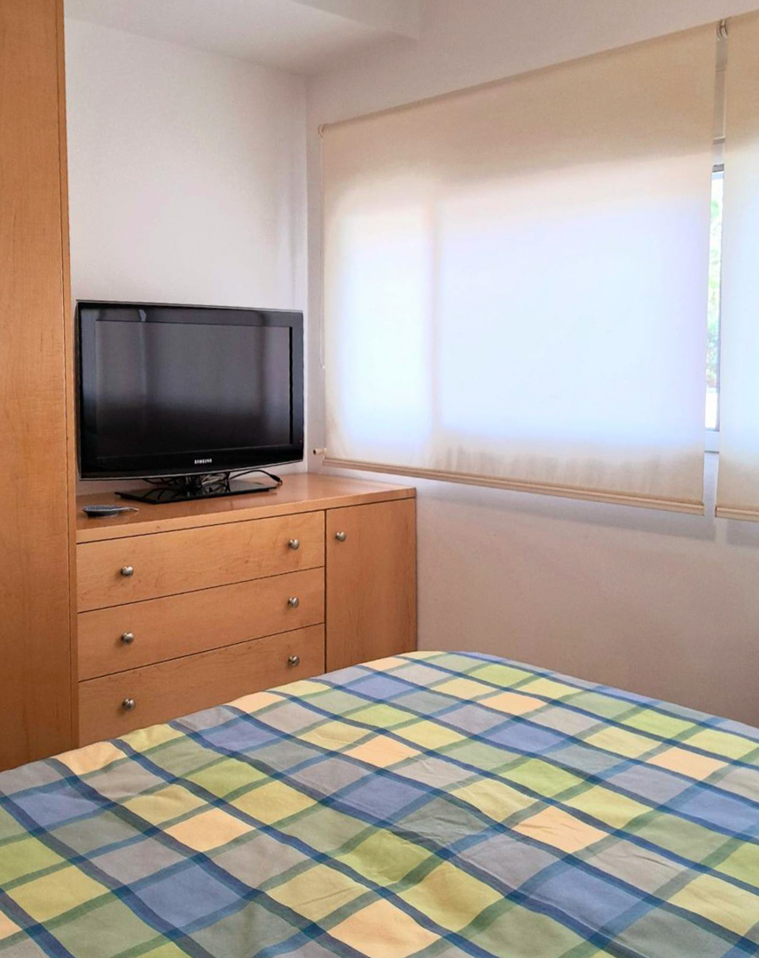 Bedroom featuring custom wood furniture, a television on a chest of drawers, and a large window with translucent roller blinds.