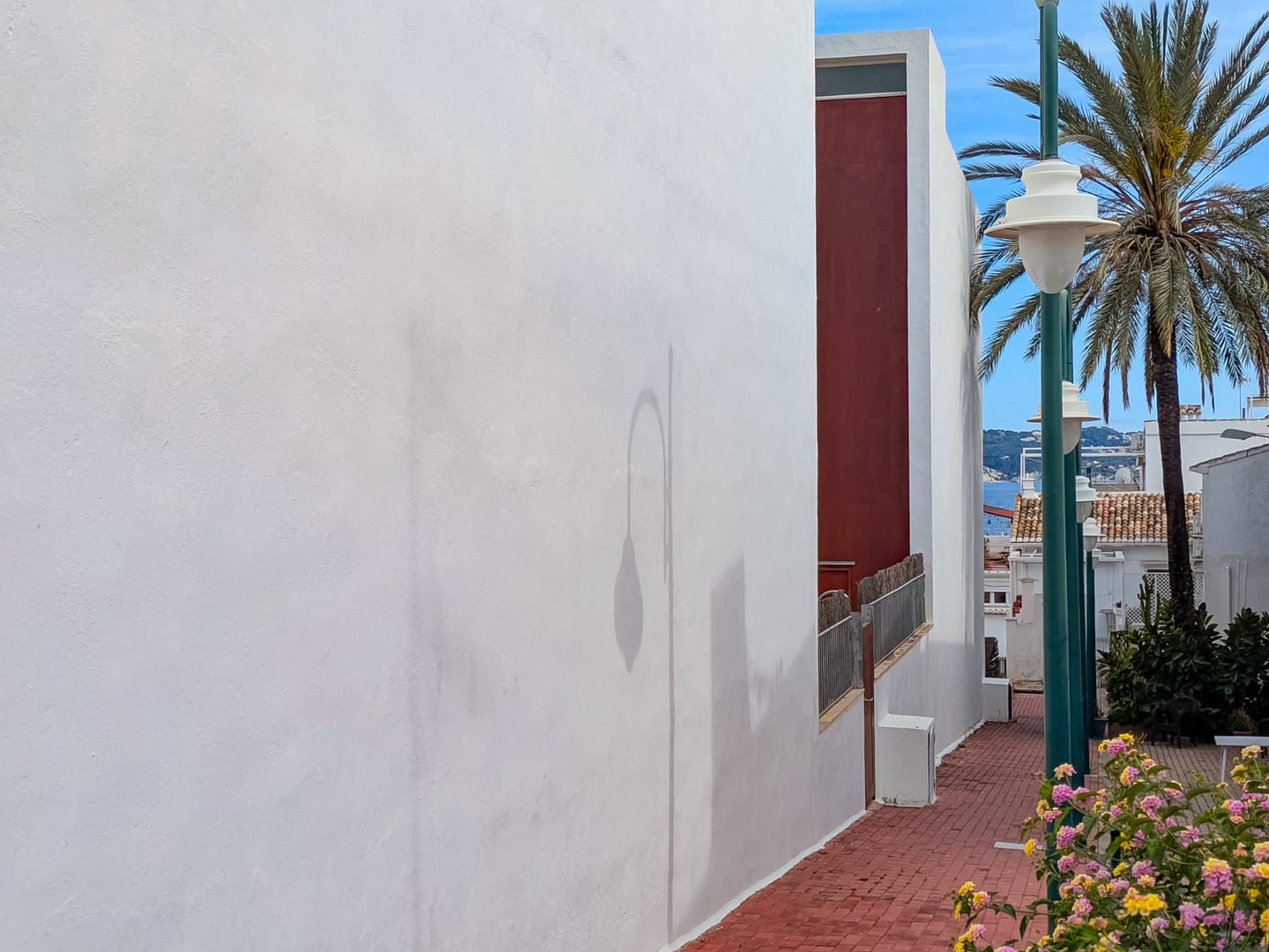 Building exterior featuring a white facade and brick pedestrian path with partial sea views, palm trees, and local flora.