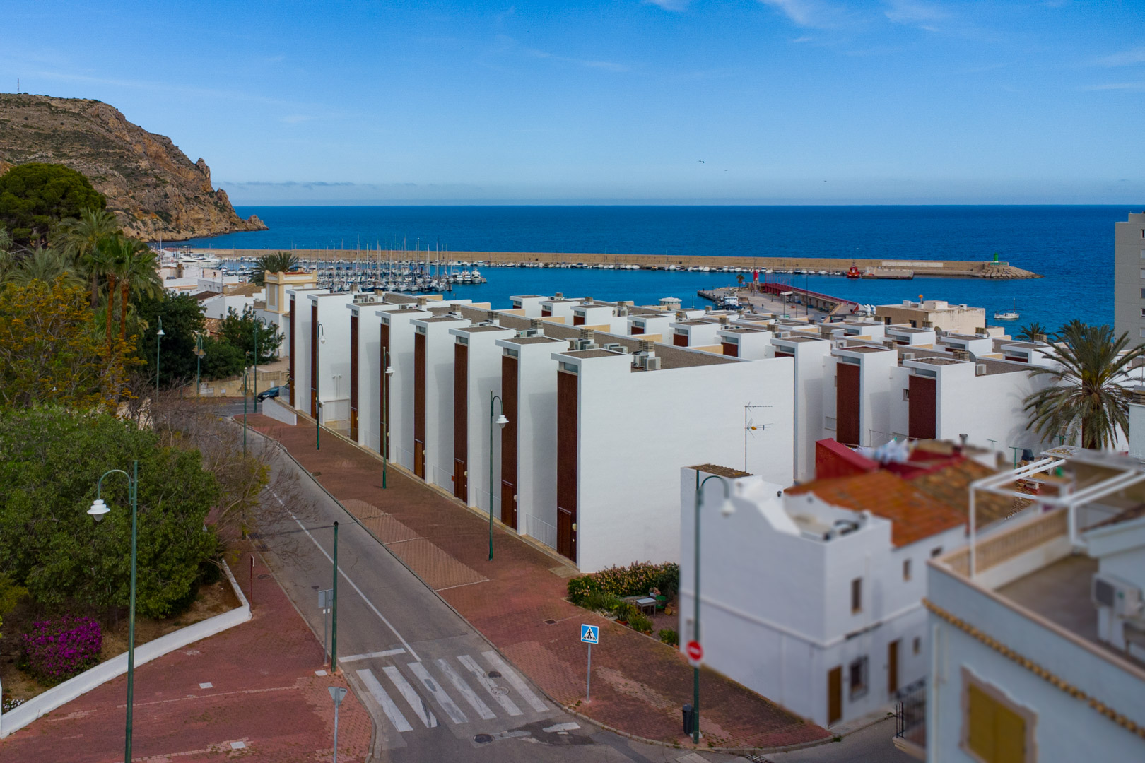 Elevated panoramic view of Jávea port and the Mediterranean Sea, featuring modern white buildings, coastal streets, and the harbor with docked boats.