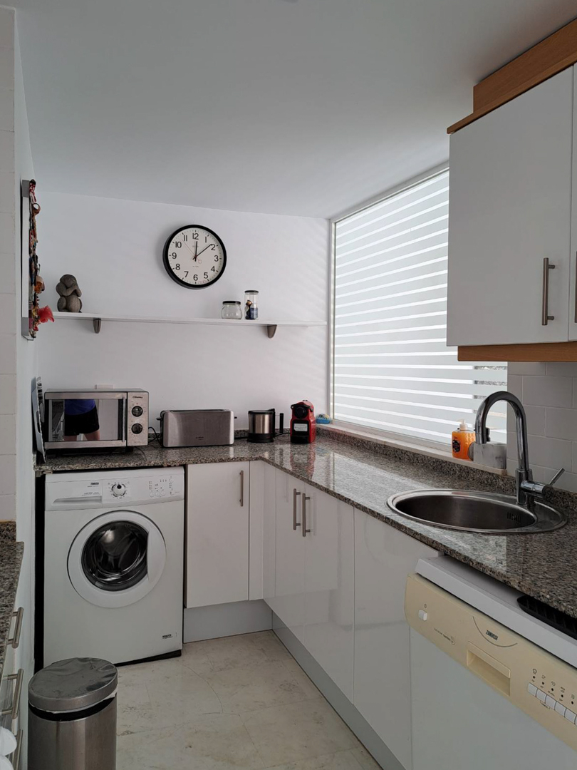 Functional L-shaped kitchen featuring granite countertops, white cabinetry, integrated appliances, and a large window with blinds for natural light.