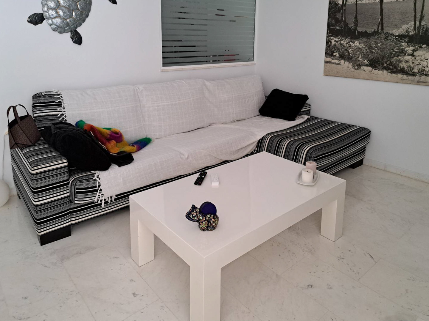 Living area featuring marble flooring, a striped L-shaped sofa with white covers, and a minimalist white coffee table in a bright, neutral setting.