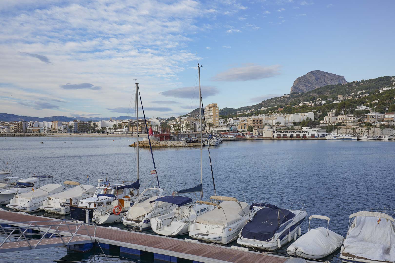Panoramic views of the Jávea marina showcasing moored leisure boats and the distinctive silhouette of the Montgó mountain under a clear sky.