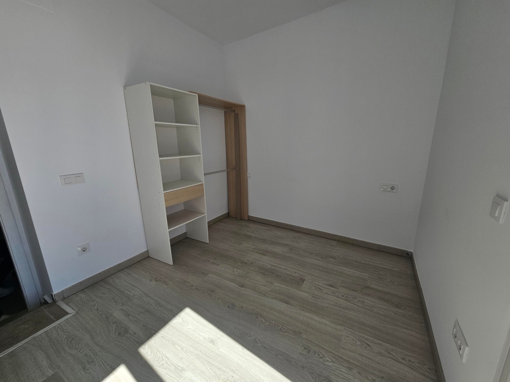 Bedroom featuring grey wood-effect flooring, white walls, and a modular open wardrobe system with white shelving and light wood accents.