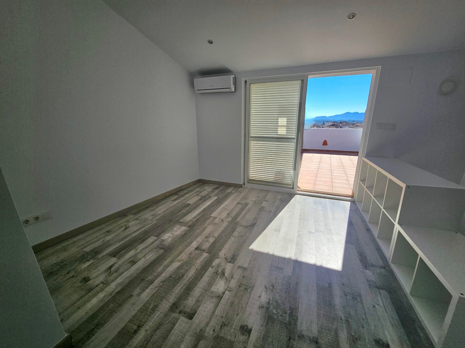 Bright office space featuring wood-effect flooring, air conditioning, and sliding doors opening onto a private terrace with mountain views.