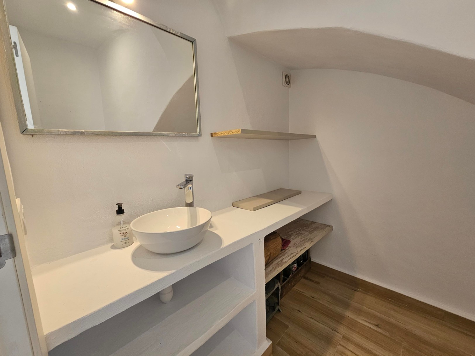 Ground floor guest toilet featuring a white vessel sink on a built-in vanity with open shelving. Includes a sloped ceiling, wood-effect flooring, and a framed mirror.