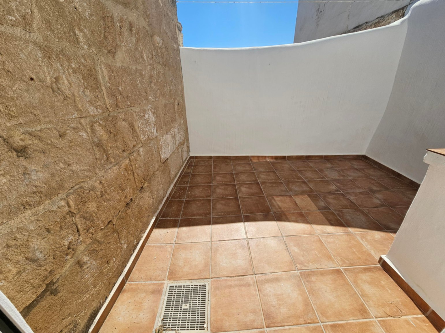 Private outdoor patio featuring terracotta floor tiles, an original natural stone wall, and clean white plastered finishes under an open sky.
