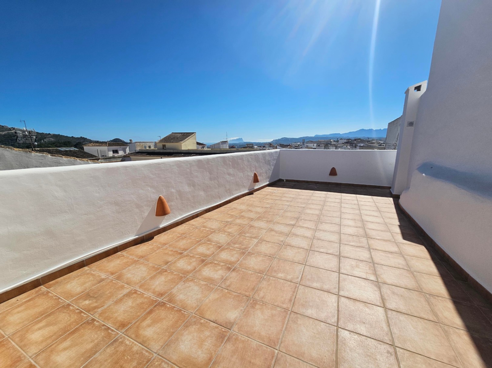 Rooftop terrace featuring terracotta tiling, whitewashed walls, and panoramic views of the town, mountains, and the distant sea.