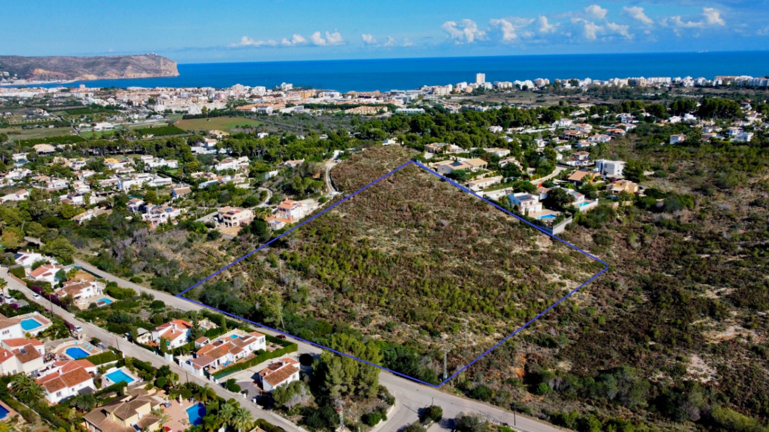 Aerial view of the 17,272 m² plot in Jávea, outlined in blue, situated within a residential area with views of the Mediterranean Sea and the coastline.