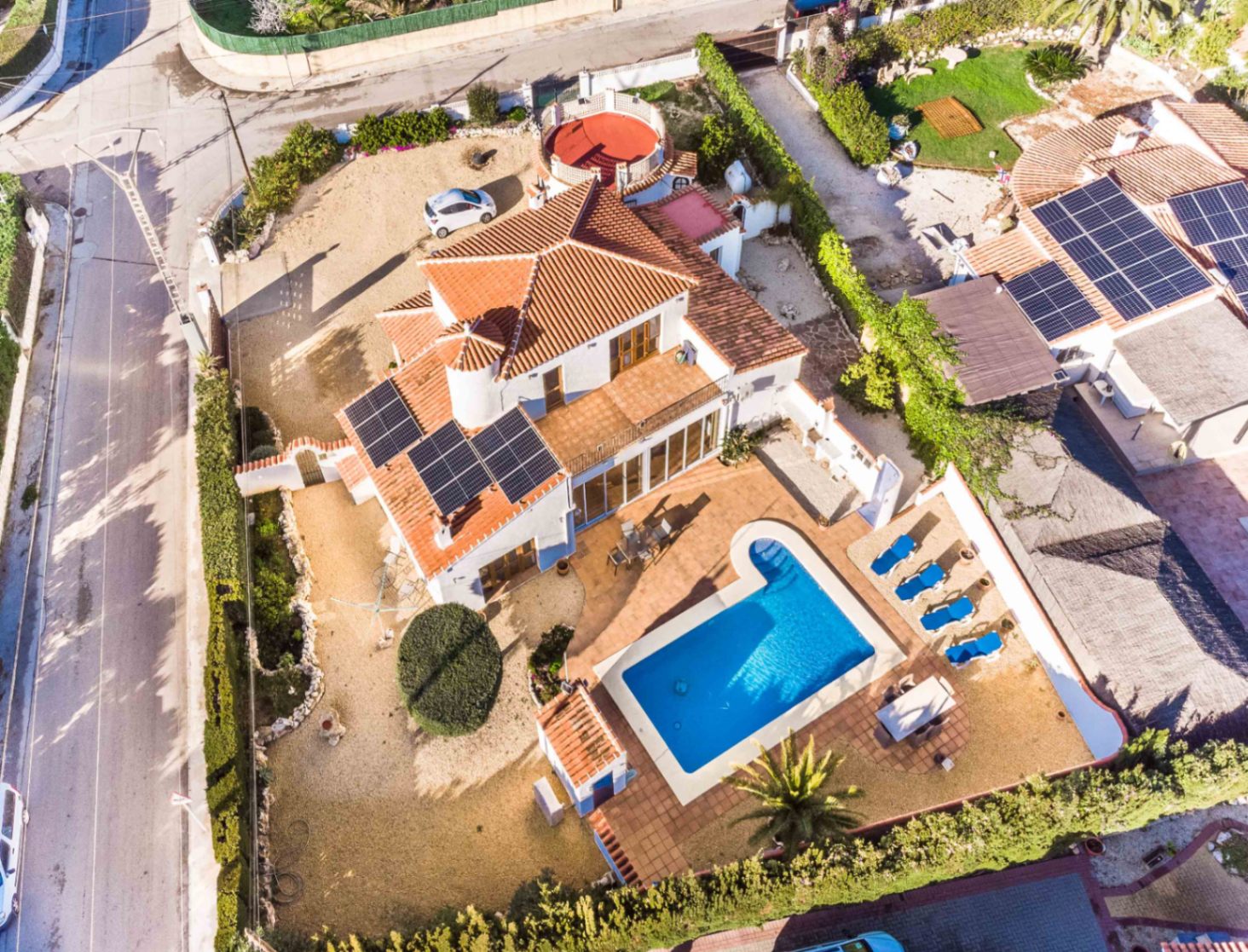 Aerial view of the villa featuring a private swimming pool, sun deck with loungers, rooftop solar panels, and the spacious corner plot layout.