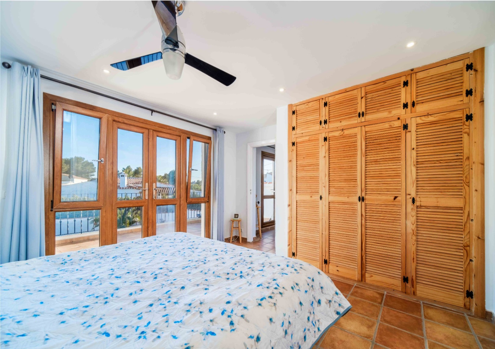 Bedroom featuring built-in wooden wardrobes, terracotta tile flooring, and large glass doors leading to a private balcony.