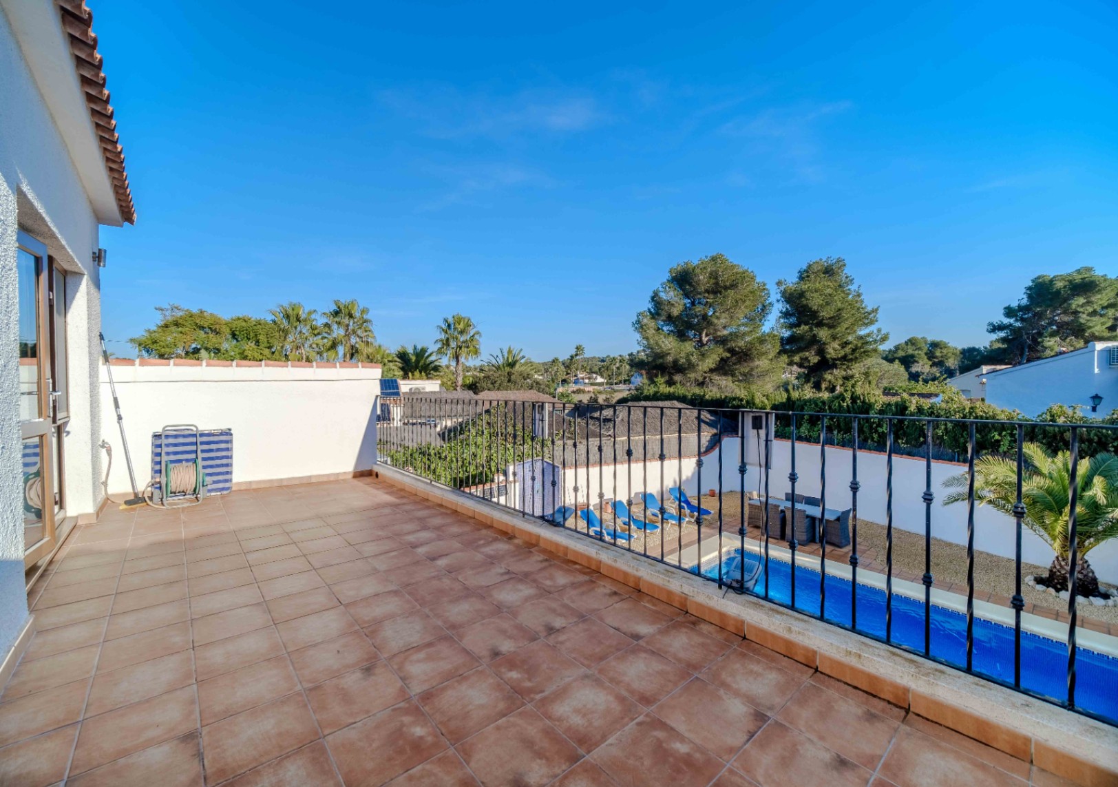 Elevated sun terrace featuring terracotta tiling and wrought iron railings, overlooking the private pool area and lush Mediterranean landscape.