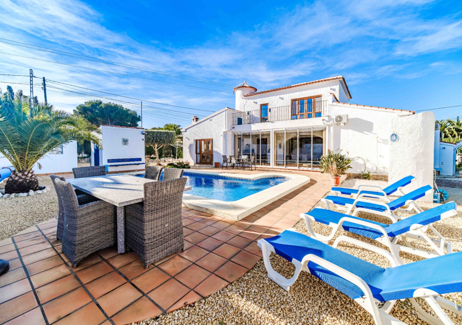 Exterior view featuring a private pool, terracotta terrace with outdoor dining area, and blue sun loungers against a white Mediterranean facade.