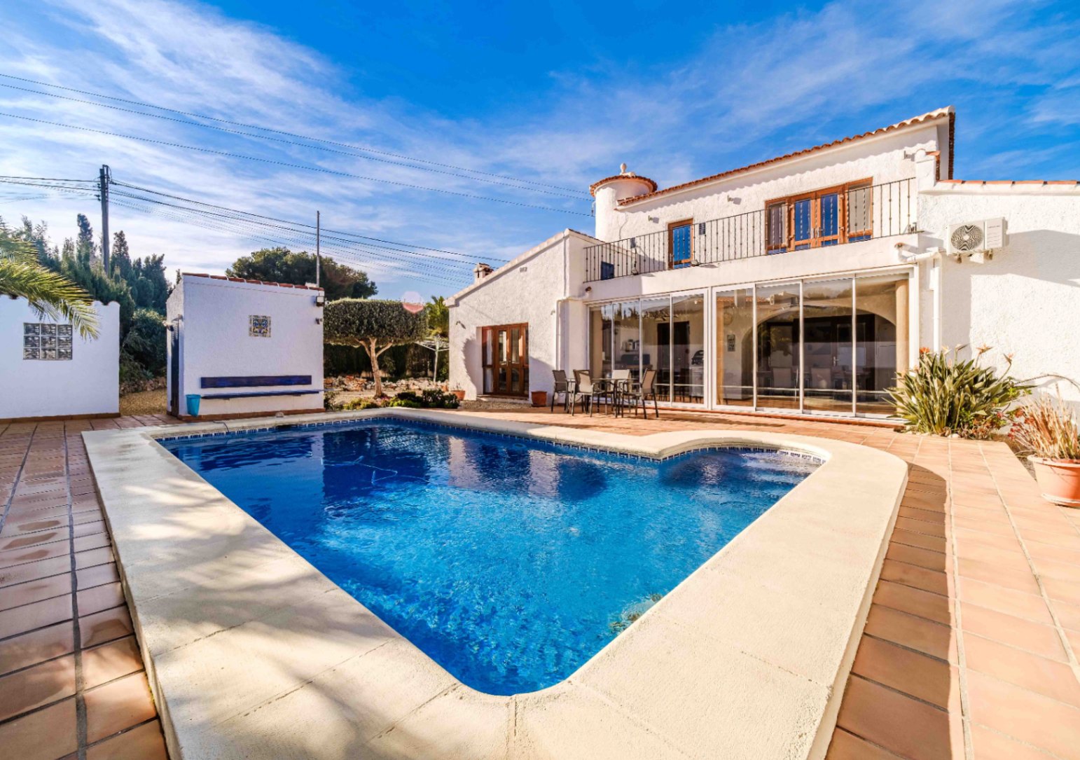 Outdoor swimming pool with integrated steps, surrounded by a terracotta tile terrace and the villa's white facade featuring a glass-enclosed lounge.