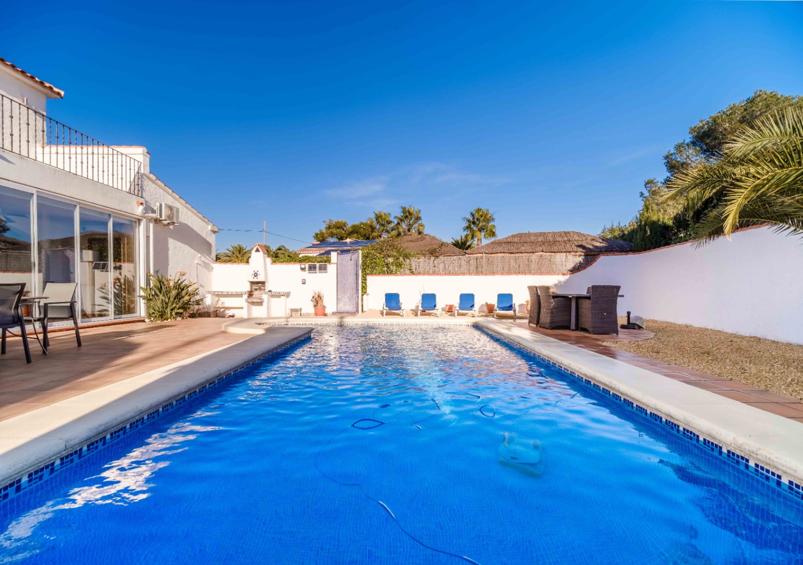 Rectangular blue-tiled swimming pool featuring a terracotta sun terrace, integrated outdoor barbecue area, and solar panels visible on the roofline.
