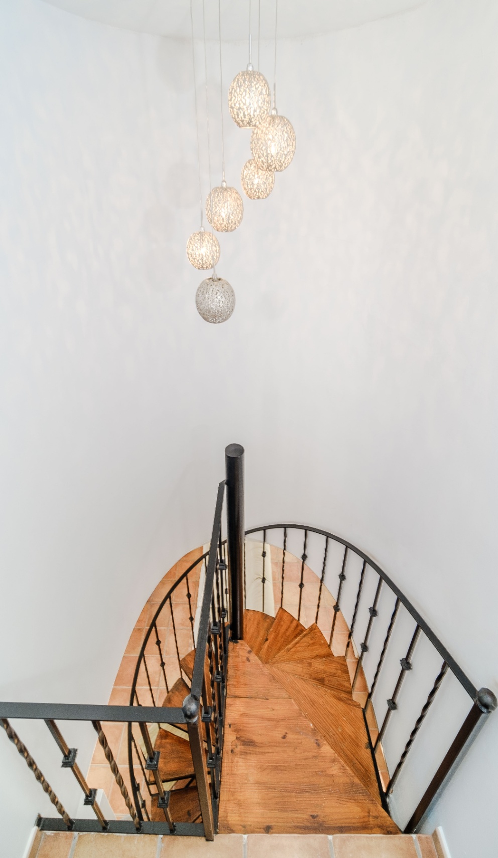 Spiral staircase featuring solid wood treads and a black wrought iron railing, illuminated by a cluster of decorative spherical pendant lights.