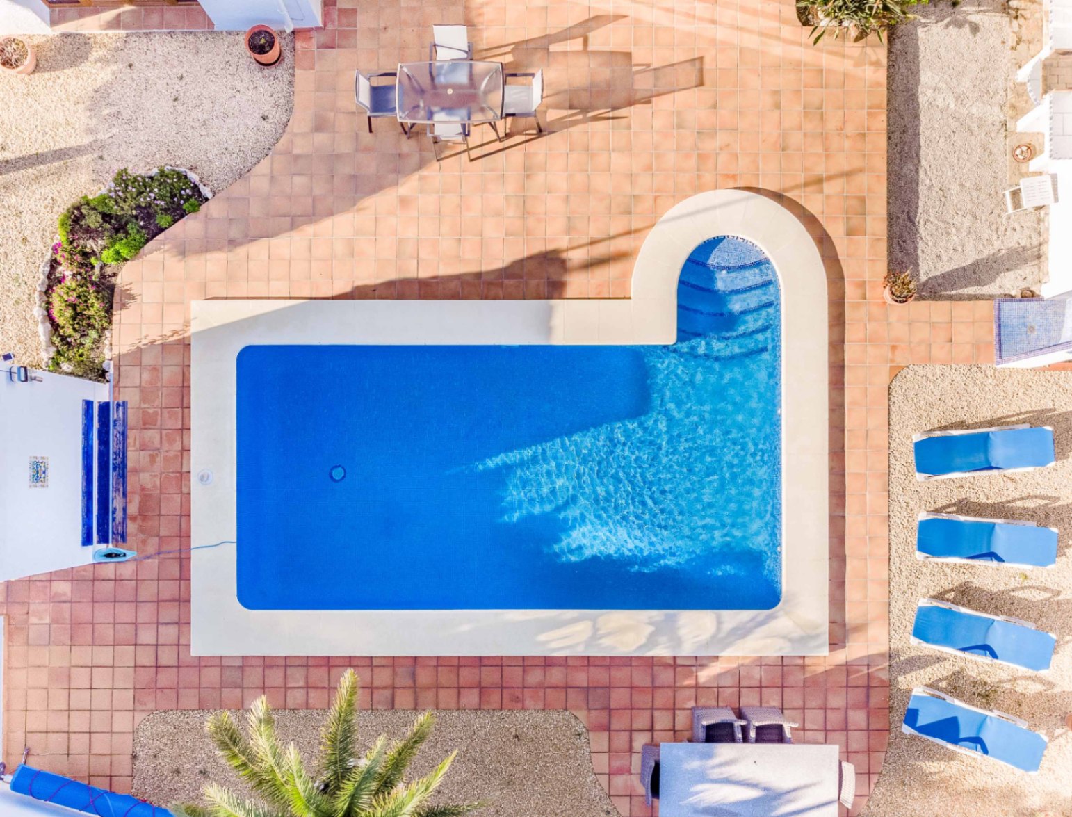 Zenithal view of the rectangular swimming pool featuring a curved Roman entry, surrounded by terracotta tiling, sun loungers, and outdoor dining areas.