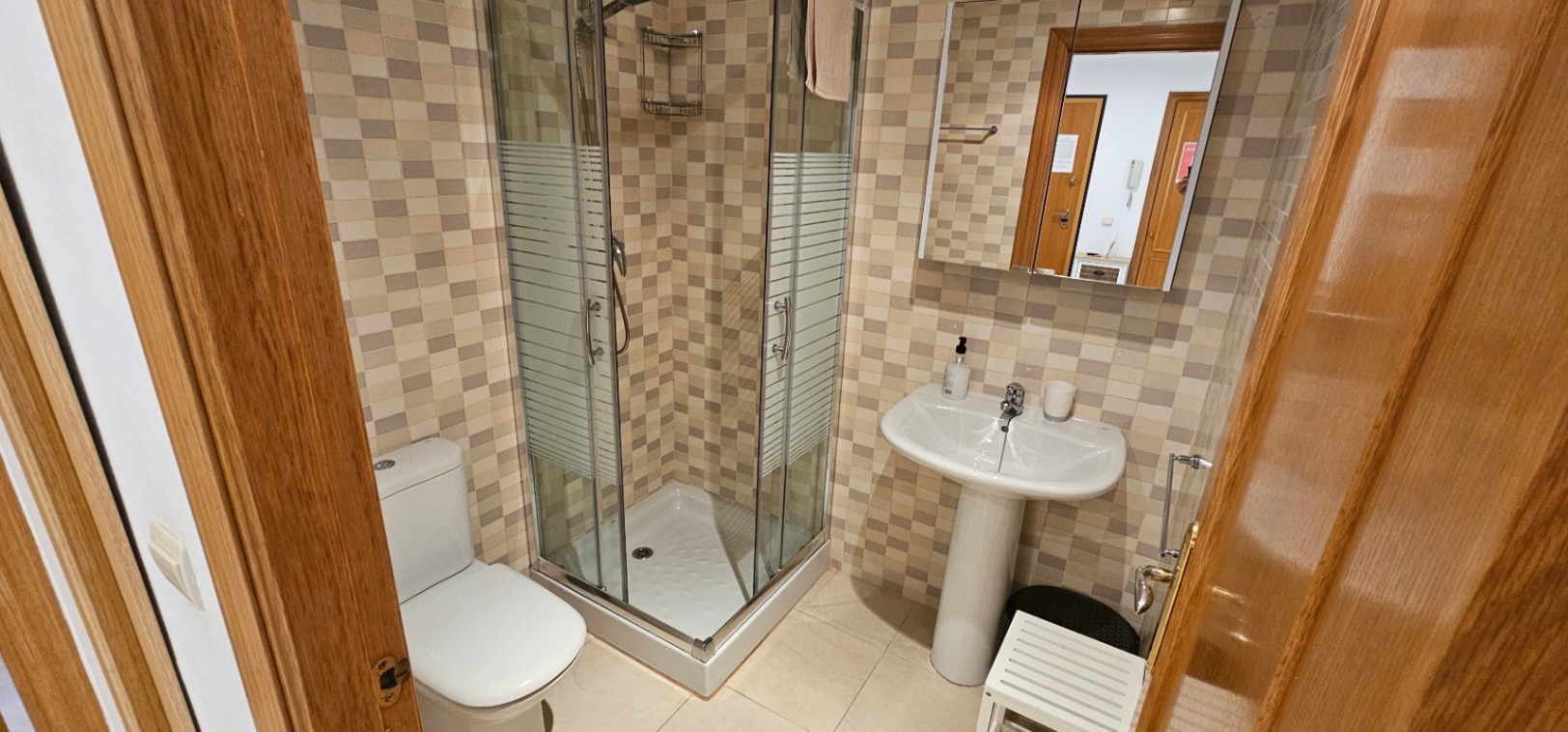 Bathroom featuring a corner glass shower enclosure, a white pedestal sink, and walls finished with earth-toned mosaic tiles.